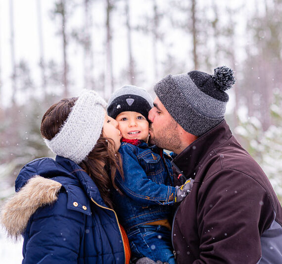 Parents on either side of their son kissing him on the cheek.