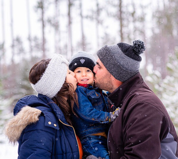 Parents on either side of their son kissing him on the cheek.