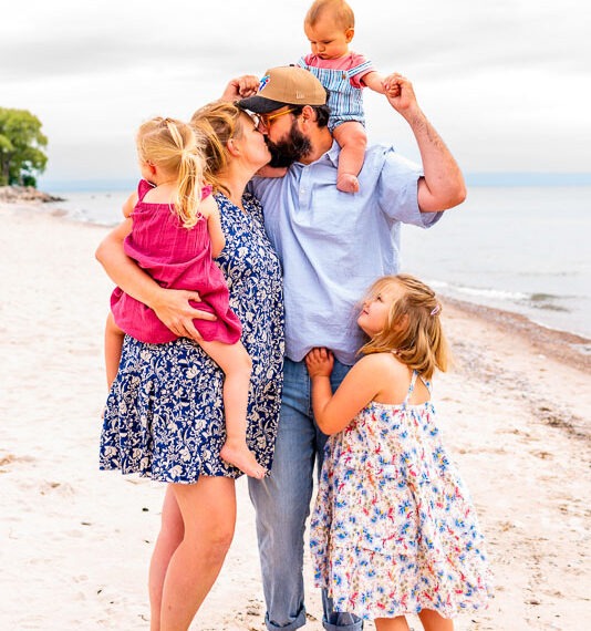 Parents kissing with their 3 children watching on the beach.