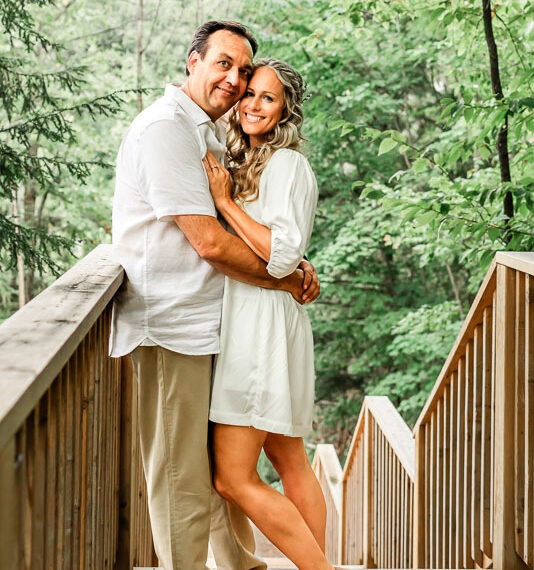 Engaged couple embraced on a bridge in the forest.