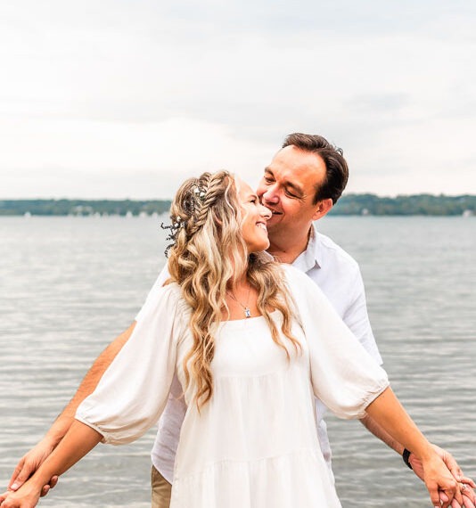 Engaged couple holding hands by a lake.