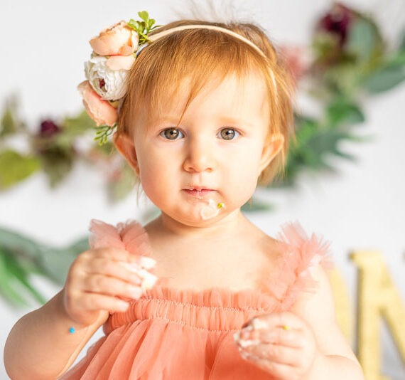 Baby having portrait taken while smashing their first birthday cake.