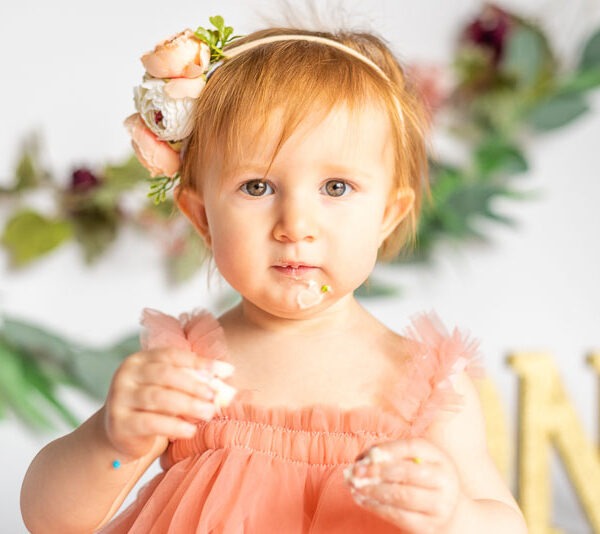 Baby having portrait taken while smashing their first birthday cake.