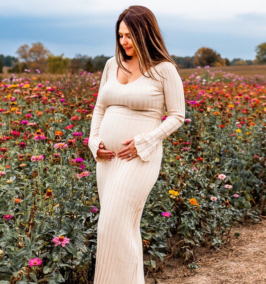 Pregnant woman holding her belly beside a field of flowers.