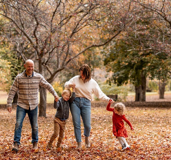 Parents with their two children playing in the woods during fall.