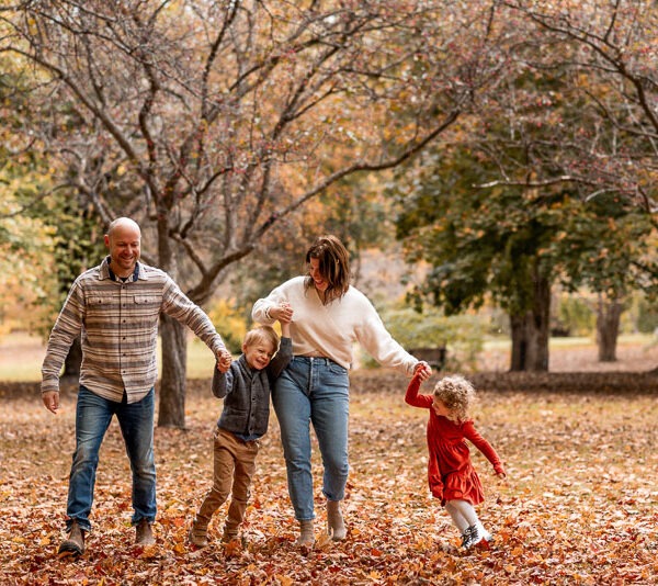 Parents with their two children playing in the woods during fall.