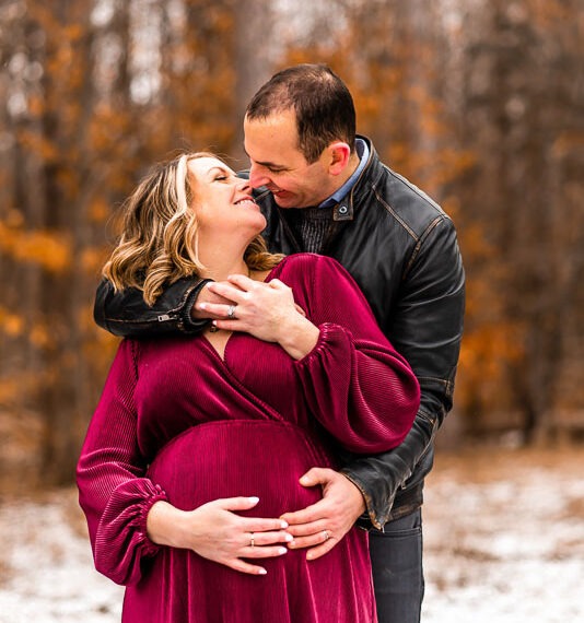 Couple holding pregnant belly in the snow woods.