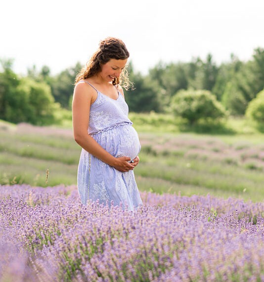 Pregnant woman holding her belly while standing in a field of lavender.