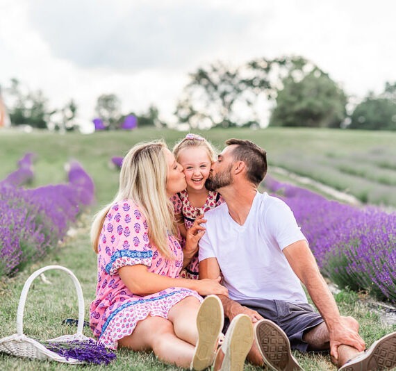 Parents on either side of their daughter kissing her on the cheek in lavender field.