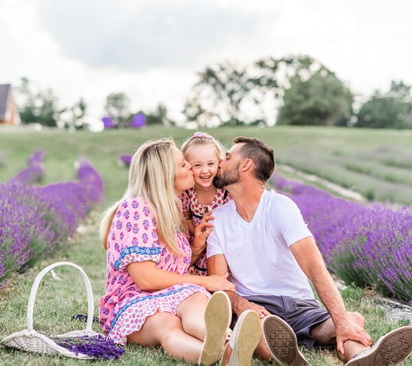 Parents on either side of their daughter kissing her on the cheek in lavender field.