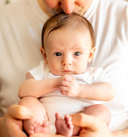 Father holding newborn baby kissing the top of their head.