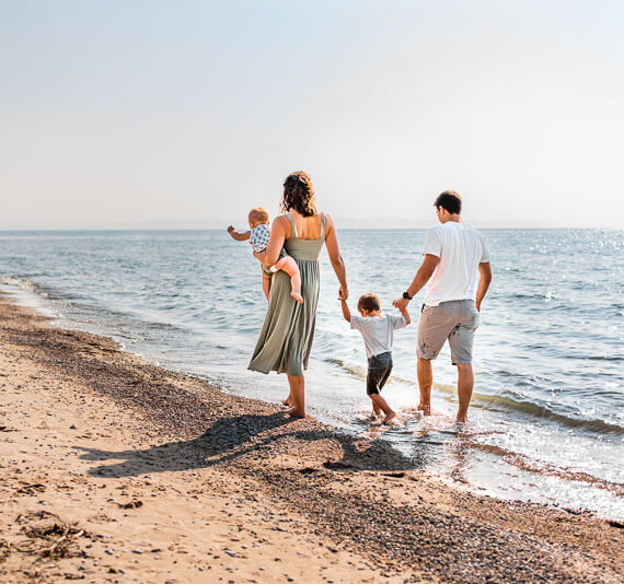 Parents with two children walking along a lake with their feet in the water.