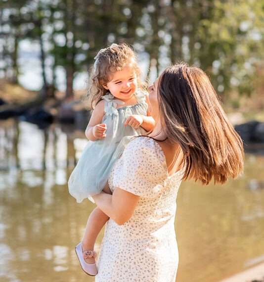 Mother holding her daughter by a lake laughing.