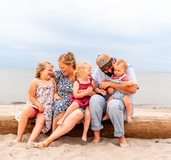 Parents with their 3 children sitting on a log at the beach.