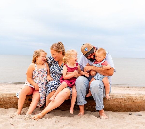 Parents with their 3 children sitting on a log at the beach.