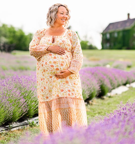 Pregnant woman holding her belly smiling in a lavender field.