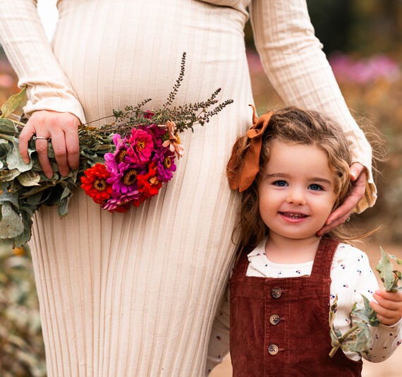 Pregnant mother with her young daughter holding flowers.