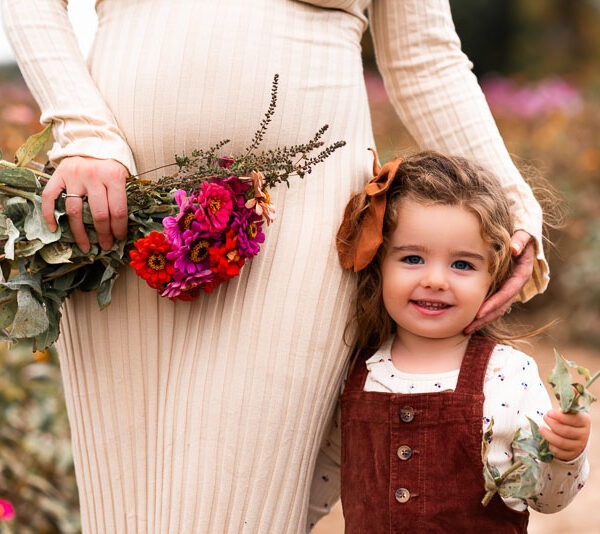 Pregnant mother with her young daughter holding flowers.