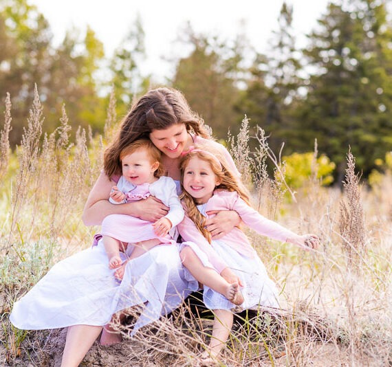 Mother with her two children sitting in the grass infront of the woods.