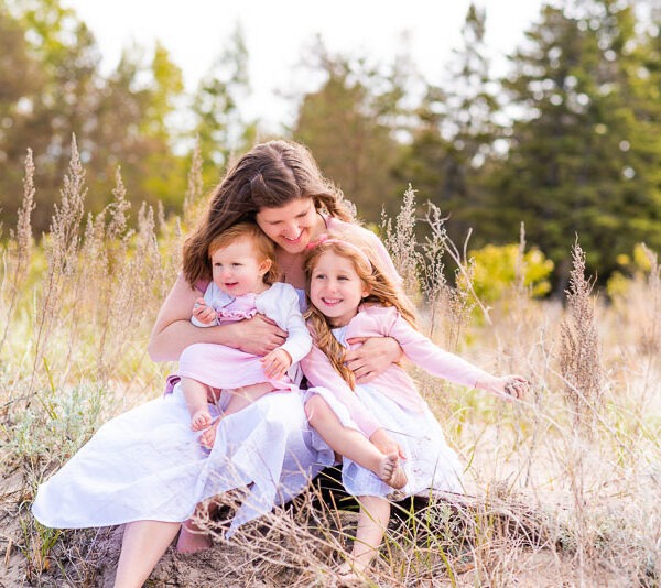 Mother with her two children sitting in the grass infront of the woods.