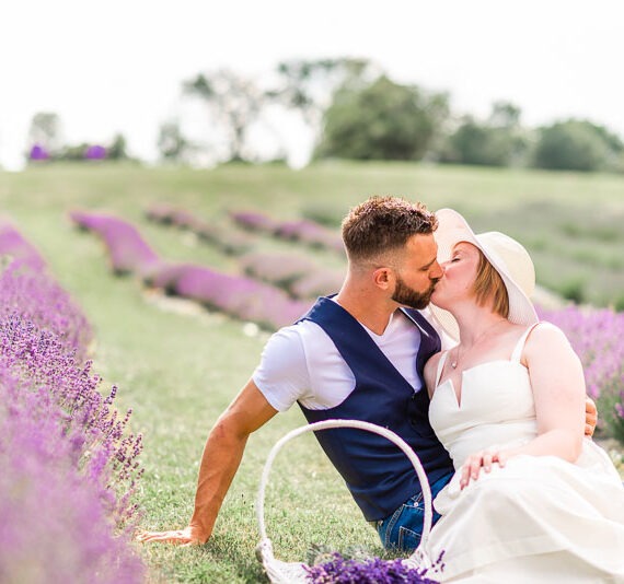 Engaged couple sitting in a lavender field kissing.