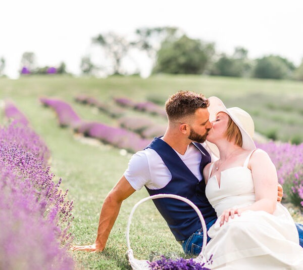 Engaged couple sitting in a lavender field kissing.