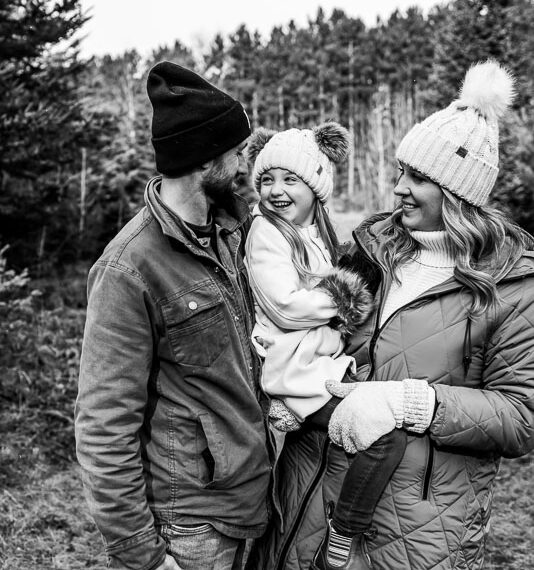 Parents with their daughter in the woods in their winter gear.