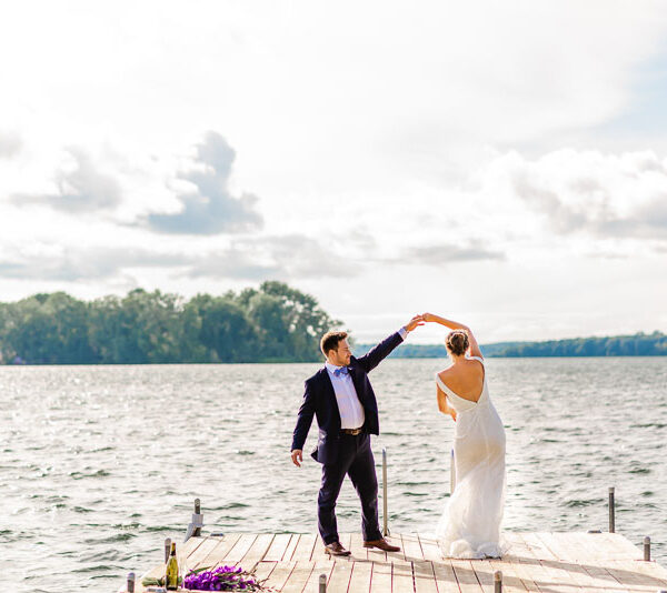 Newlyweds dancing on a dock beside a lake.