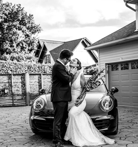 Newlyweds sharing a moment infront of a luxury car.