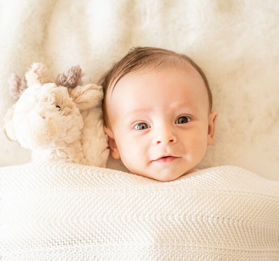 Newborn cuddled up with a stuffed animal under a blanket.